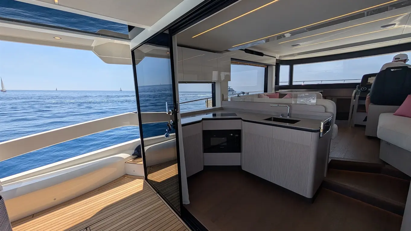 Modern yacht interior with a kitchenette, open to the sea view, featuring stylish furnishings and a captain at the helm.